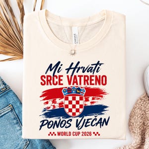 May include: Cream-colored t-shirt with the Croatian flag and text in blue and red. The shirt features the words "Mi Hrvati SRCE VATRENO PONOS VJEČAN WORLD CUP 2026" in a stylized font, celebrating Croatian pride.