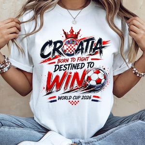 May include: White t-shirt with a Croatian soccer theme. The design features the word "CROATIA" in black and red, a crown, and a soccer ball. Text includes "BORN TO FIGHT, DESTINED TO WIN" and "WORLD CUP 2026".