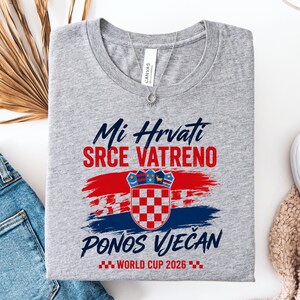 May include: A gray t-shirt with the text "Mi Hrvati SRCE VATRENO PONOS VJEČAN WORLD CUP 2026" in blue and red. The shirt features a Croatian flag design. A silver necklace is visible.