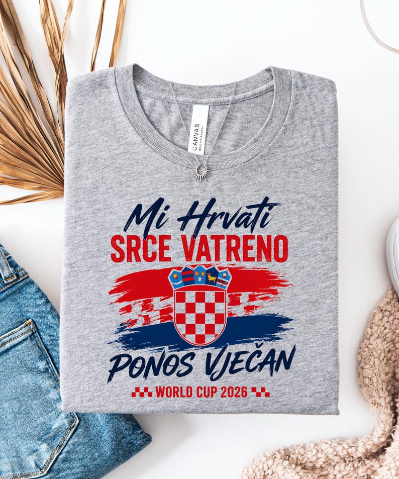 May include: A gray t-shirt with the text "Mi Hrvati SRCE VATRENO PONOS VJEČAN WORLD CUP 2026" in blue and red. The shirt features a Croatian flag design. A silver necklace is visible.