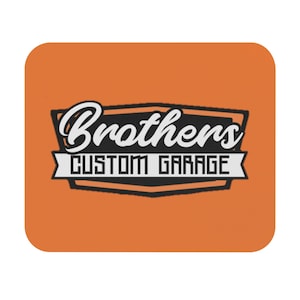 May include: An orange square coaster with the words "Brothers Custom Garage" in a black and white design. The text is in a stylized font, with "Brothers" in cursive and "Custom Garage" in a block font.