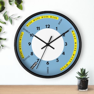 May include: A round wall clock with a black frame and a light blue face. The clock features black hands and a white center. The face has the words "Work," "Coffee," "Brunch," "Shower," "Dinner," and "Break" printed on it.
