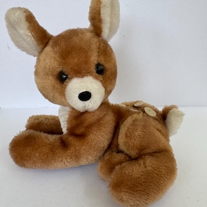 Puede incluir: Un peluche de ciervo marr&oacute;n en posici&oacute;n de reposo. El ciervo tiene detalles blancos en las orejas, el pecho y la cola. Tiene ojos negros y una nariz negra. El juguete est&aacute; hecho de material suave y difuso.