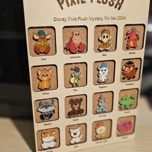 May include: Wooden display featuring Disney Pixie Plush Mystery Pins. The display includes pins of various Disney characters like Gus, Sebastian, Abu, and Mushu. The text "Disney Pixie Plush Mystery Pin Set 2024" is visible.