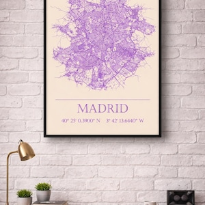 Op de afbeelding: Een ingelijste print met een paarse kaart van Madrid. Het stratennetwerk is gedetailleerd zichtbaar. Het woord "MADRID" staat onder de kaart, samen met de coördinaten 40° 25' 0.3900" N 3° 42' 13.6440" W.