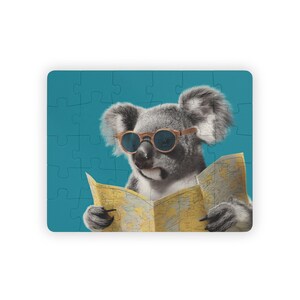 Puede incluir: Un rompecabezas con un koala con gafas de sol leyendo un mapa. El koala es gris con una nariz y orejas de color marrón claro. El rompecabezas tiene un fondo azul.