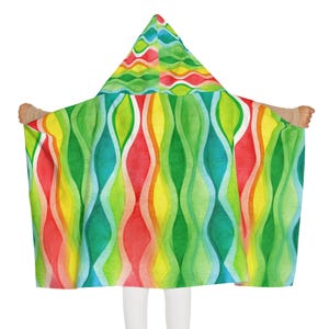 May include: A hooded blanket featuring a vibrant watercolor pattern of vertical wavy lines in shades of red, orange, yellow, lime green, and teal. The design includes a pointed hood and a wide, flowing rectangular body with a repeating wave motif.