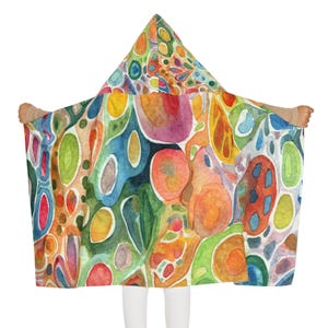 May include: A hooded blanket featuring a vibrant watercolor pattern of abstract organic shapes in shades of red, orange, yellow, green, and blue. The design covers the entire surface, including the pointed hood, with soft, blended edges.