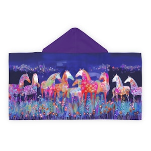 May include: A hooded towel featuring a vibrant, multi-colored illustration of several horses standing in a field of flowers against a dark blue night sky. The hood is a solid deep purple, while the main body displays a whimsical, colorful pattern.