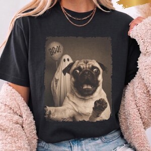 Könnte beinhalten: Ein schwarzes Kurzarm-T-Shirt mit einem Grafikdruck eines Mopses, der nach vorne greift, und einem Geist im Hintergrund, der einen Ballon mit der Aufschrift BOO! hält. Das Shirt hat einen Rundhalsausschnitt und einen rechteckigen Rand.