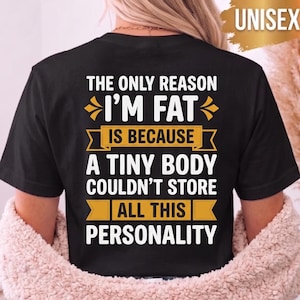 Könnte beinhalten: Ein schwarzes T-Shirt mit kurzen Ärmeln und weißem sowie gelbem Text, der lautet: THE ONLY REASON I'M FAT IS BECAUSE A TINY BODY COULDN'T STORE ALL THIS PERSONALITY. Das Design enthält dekorative gelbe grafische Elemente über und unter dem Text.