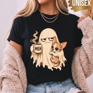 Może przedstawiać: Czarny t-shirt z grafiką przedstawiającą beżowego ducha z niezadowoloną miną, trzymającego parujący kubek z napisem MEH i obejmującego małego brązowo-białego psa rasy chihuahua. Wzór znajduje się na środku klatki piersiowej odzieży.