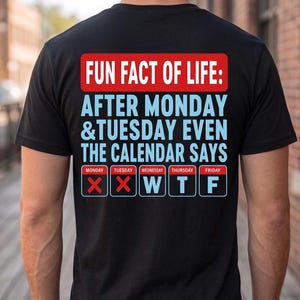 Puede incluir: Una camiseta negra con un gráfico en la parte posterior con el texto: FUN FACT OF LIFE: AFTER MONDAY & TUESDAY EVEN THE CALENDAR SAYS. Debajo, una cuadrícula de calendario muestra lunes y martes marcados con X rojas, seguidos de W, T, F.