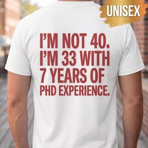 May include: A white short-sleeved t-shirt with red text on the back that reads: I'M NOT 40. I'M 33 WITH 7 YEARS OF PHD EXPERIENCE. A gold-coloured brushstroke graphic in the upper right corner contains the white text UNISEX.