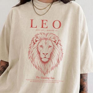Leo zodiac graphic t-shirt on Comfort Colors 1717 in Ivory featuring a vintage red line art lion illustration with "The Guiding Sun" quote, worn by a woman against a neutral background.