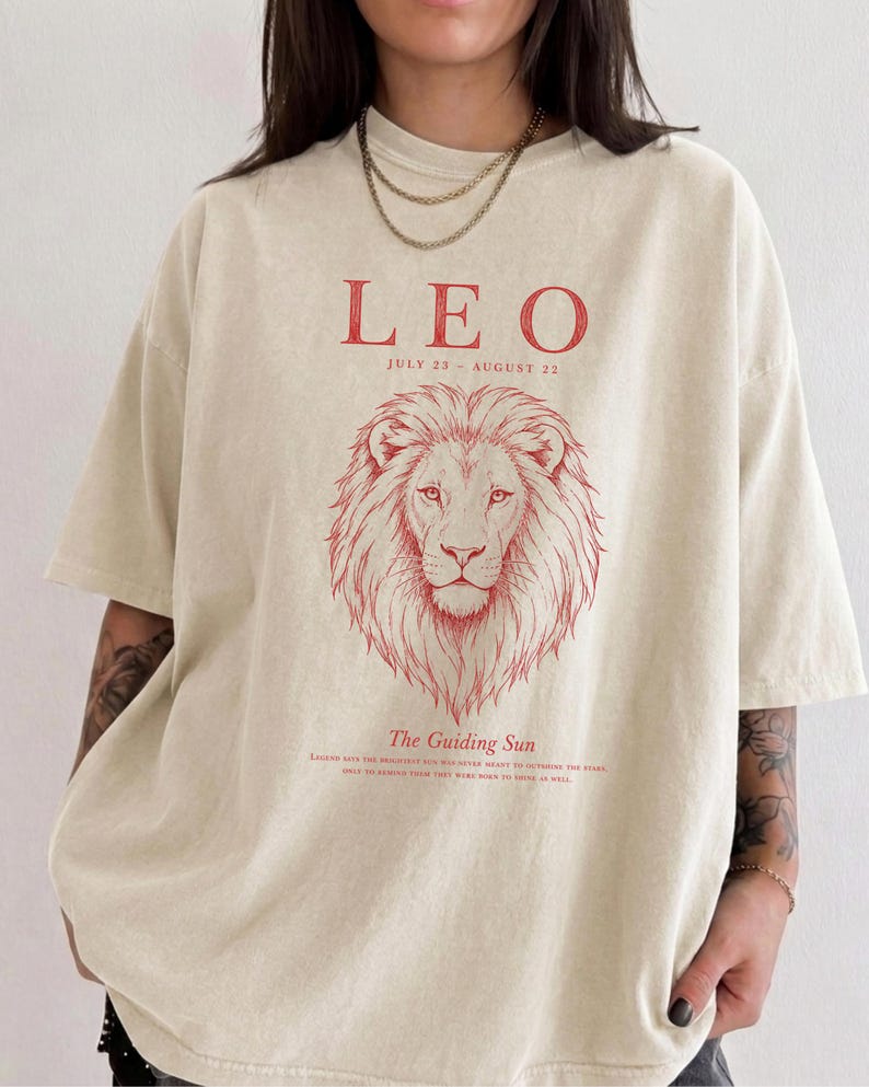 Leo zodiac graphic t-shirt on Comfort Colors 1717 in Ivory featuring a vintage red line art lion illustration with "The Guiding Sun" quote, worn by a woman against a neutral background.