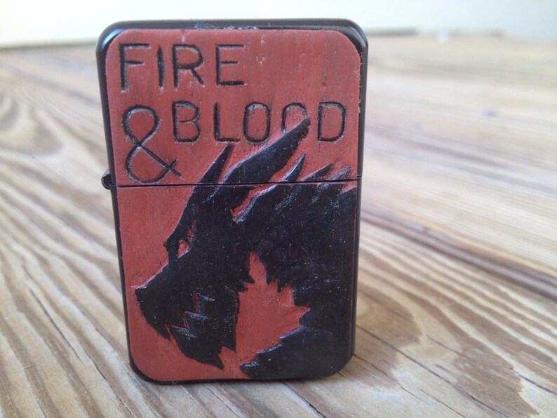 Puede incluir: Un encendedor negro y rojo con las palabras "FIRE & BLOOD" y un dise&ntilde;o de drag&oacute;n.