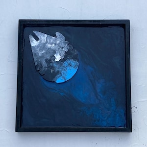 May include: A framed artwork featuring a stylized Millennium Falcon design. The artwork uses shades of blue, white, and black to create a galaxy-like effect. The design is set against a dark blue background within a black frame.