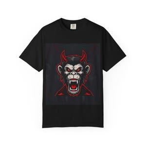 May include: Black t-shirt featuring a devil monkey graphic. The design includes a red-horned monkey with an open mouth, red eyes, and a dark background. The shirt is made of a soft material.