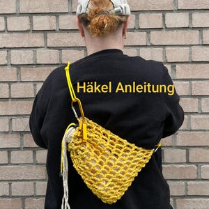 Könnte beinhalten: Eine gelbe gehäkelte Netztasche mit Kordelzug, ausgestattet mit einer leuchtend gelben Kordel und einem goldfarbenen Metallkarabiner. Der Text "Häkel Anleitung" ist in gelben Buchstaben auf dem schwarzen Oberteil zu sehen.