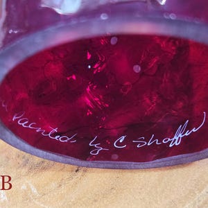Underside of red glass shade labeled B showing white painted signature C. Shaffer