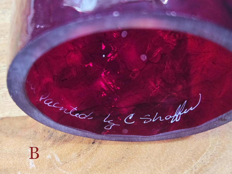 Underside of red glass shade labeled B showing white painted signature C. Shaffer