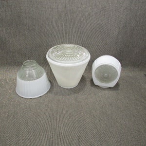 Op de afbeelding: Drie vintage glazen lampenkappen. De lampenkappen zijn wit en helder, met geribbelde en patroonontwerpen. Eén kap heeft een kleine, uitlopende vorm, een andere een kegelvorm en de derde een afgeronde vorm.