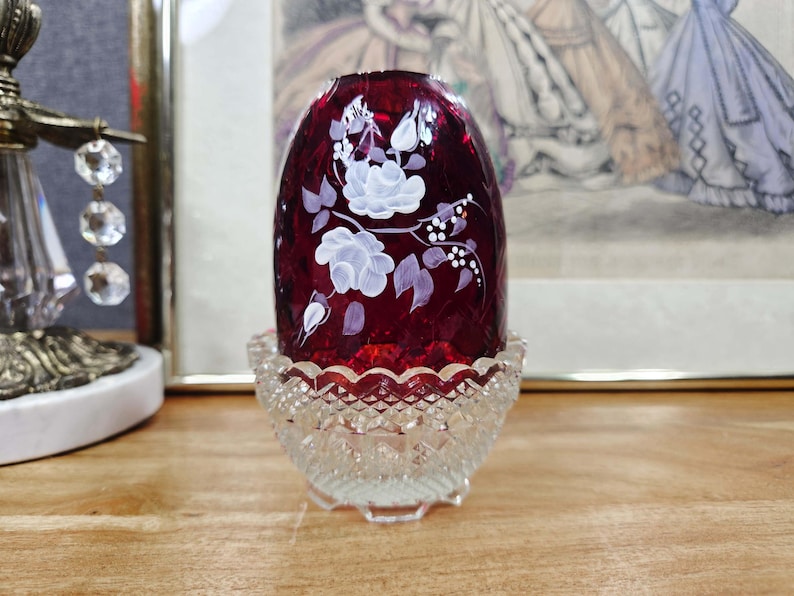 Ruby Red glass fairy lamp with white painted flowers with a clear pressed glass base on a wood surface