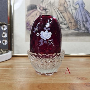 Fairy lamp labeled A with ruby red glass shade, white painted floral design, and clear pressed glass base