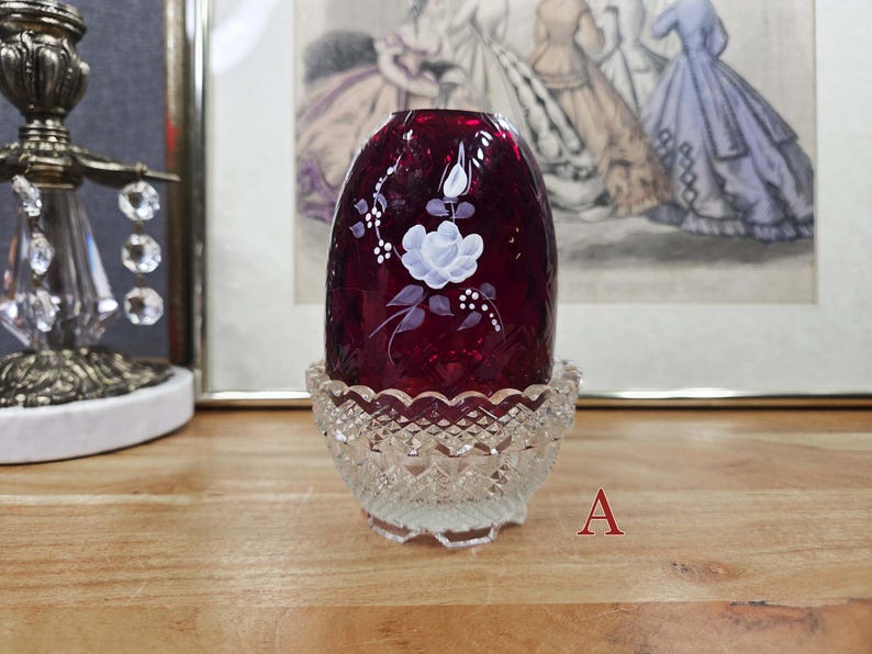 Fairy lamp labeled A with ruby red glass shade, white painted floral design, and clear pressed glass base