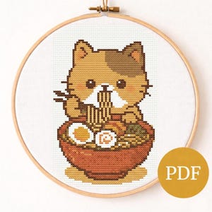 May include: A cross-stitch pattern featuring a calico cat enjoying ramen from a brown bowl. The cat is holding chopsticks and eating noodles. The design is set in a wooden embroidery hoop, with a yellow "PDF" circle in the corner.