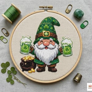 May include: Cross-stitch embroidery of a St. Patrick's Day gnome holding two green beers, a pot of gold, and wearing a green hat with shamrocks. The embroidery is in a wooden hoop.