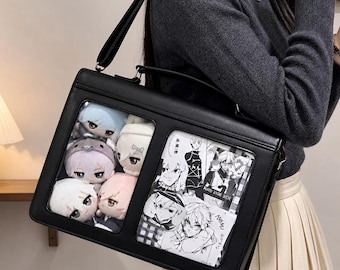 Puede incluir: Bolso mensajero negro con dos ventanas transparentes. Una ventana muestra muñecos de peluche de varios colores, mientras que la otra muestra ilustraciones de manga en blanco y negro. El bolso tiene un asa superior y una correa para el hombro.