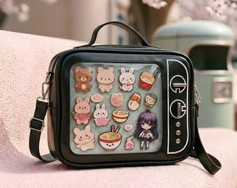 Puede incluir: Bolso negro cuadrado con asa y bandolera. La parte delantera presenta una ventana transparente que muestra varias pegatinas de personajes de dibujos animados, incluyendo osos, conejos y alimentos. El bolso tiene un diseño de TV retro con detalles en blanco.