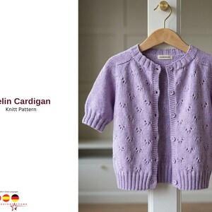 May include: A light purple knit cardigan with short sleeves, button closures, and a delicate openwork pattern. The garment is displayed on a wooden hanger. Text on the left reads "Pelin Cardigan Knitt Pattern".