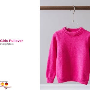 以下が含まれることがあります： 鮮やかなピンク色の女の子用プルオーバーセーターが透明なハンガーに掛けられています。セーターはクルーネックと長袖です。左側のテキストには「Nida Girls Pullover Crochet Pattern」と書かれています。