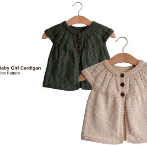 Puede incluir: Dos cárdigans para bebé niña en perchas de madera. Uno es verde oliva, el otro color crema. Ambos tienen mangas cortas, cierres de botones decorativos y el texto "Lenona Baby Girl Cardigan Knitt Pattern".