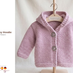 Könnte beinhalten: Ein helllila gestrickter Baby-Hoodie mit Kapuze und langen Ärmeln. Der Hoodie hat zwei große Knöpfe und wird an einem Holzbügel präsentiert. Der Text "Van Baby Hoodie Knitt Pattern" ist sichtbar.