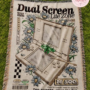 May include: A woven throw blanket featuring a graphic of a handheld game console surrounded by blue daisies. The text reads Dual Screen Lite Zone, Since 2006, Vol 03, 16 500 Yen, One to touch, one to watch, Two screens, twice the fun, and Notori Studio.