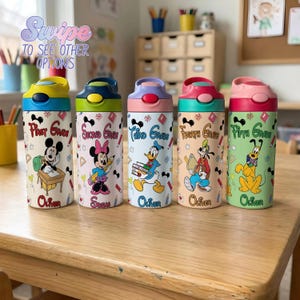 May include: Five cylindrical water bottles with flip-top lids, each featuring a Disney character, school-themed graphics, and text ranging from First Grade to Fifth Grade with names like Oliver and Susan printed on the bottom of each bottle.