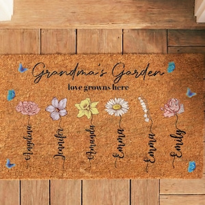May include: A rectangular doormat with the words "Grandma's Garden" and "love grows here" in black script. It features colorful flower illustrations with names below, and blue butterfly accents.