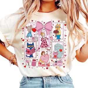 May include: Cream-colored t-shirt featuring a Valentine's Day design with cartoon characters and hearts. The design includes a large pink bow, a mouse, Arthur, Pete the Cat, and other characters. The words "Time & My Valentine" are also visible.