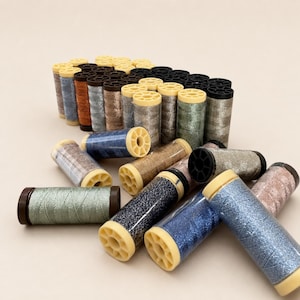 May include: A collection of metallic sewing thread spools in various colors including blue, silver, copper, gold, and black. The spools are arranged in a group with some standing upright and others lying horizontally, featuring plastic ends.
