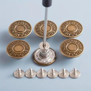 May include: A set of round brass-colored metal buttons with the text HENG SHENG JEANS embossed on the surface. The set includes several button caps, one button being installed with a metal tool, and six small silver-colored metal screw backs.