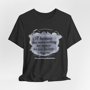 Op de afbeelding: Donkergrijs t-shirt met een citaat van Henry Ford: "Een bedrijf dat niets anders maakt dan geld, is een slecht bedrijf." Het citaat staat in een lichtblauw wolkachtig ontwerp met een stadsgezicht illustratie.