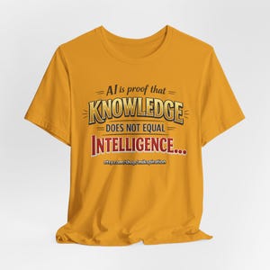 May include: Mustard yellow t-shirt with the text "AI is proof that KNOWLEDGE DOES NOT EQUAL INTELLIGENCE..." in a bold, stylized font. The Etsy shop URL is printed at the bottom of the shirt.