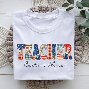 Könnte beinhalten: Weißes T-Shirt mit dem Wort "TEACHER" in einem Patchwork-Design mit roten, weißen und blauen Mustern. Unter dem Wort "TEACHER" steht der Text "Custom Name" in einer Schreibschrift.