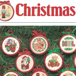 May include: A collection of 25 Christmas ornament cross-stitch patterns featuring various festive themes, including a snowman, a gingerbread house, a stocking, a wreath, a bell, a candy cane, a birdhouse, a nativity scene, a nutcracker, a cat, a train, a Father Christmas, a tree, a goose, and more. The patterns are printed on white paper with red borders.