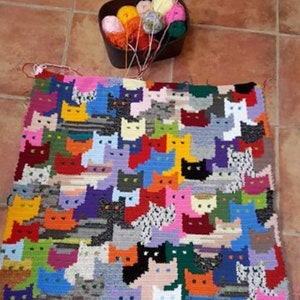 May include: A colorful crocheted blanket featuring a pattern of cats in various colors and designs. The blanket is made with different colored yarn and is a unique and handmade piece.