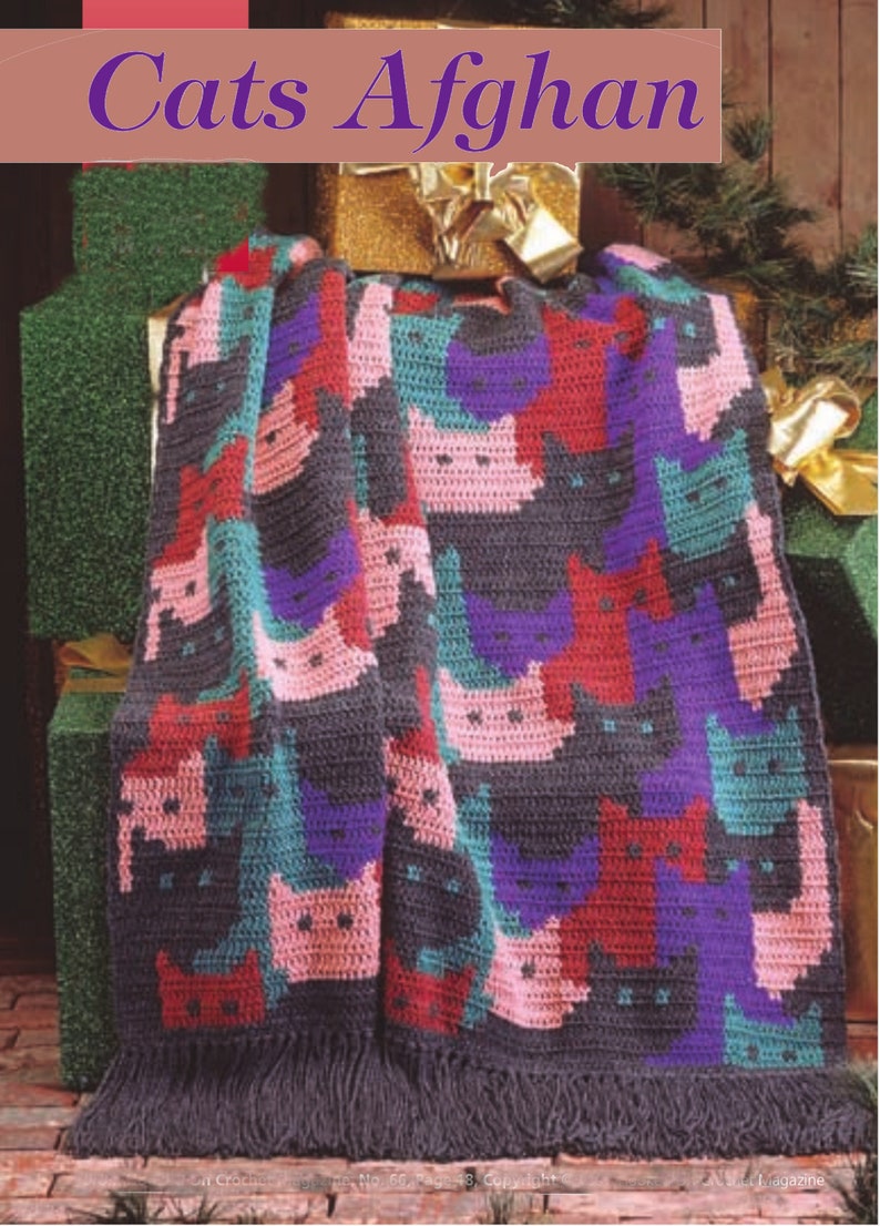 May include: A crocheted blanket with a pattern of cats in pink, red, purple, and teal on a gray background. The blanket has a fringe border.